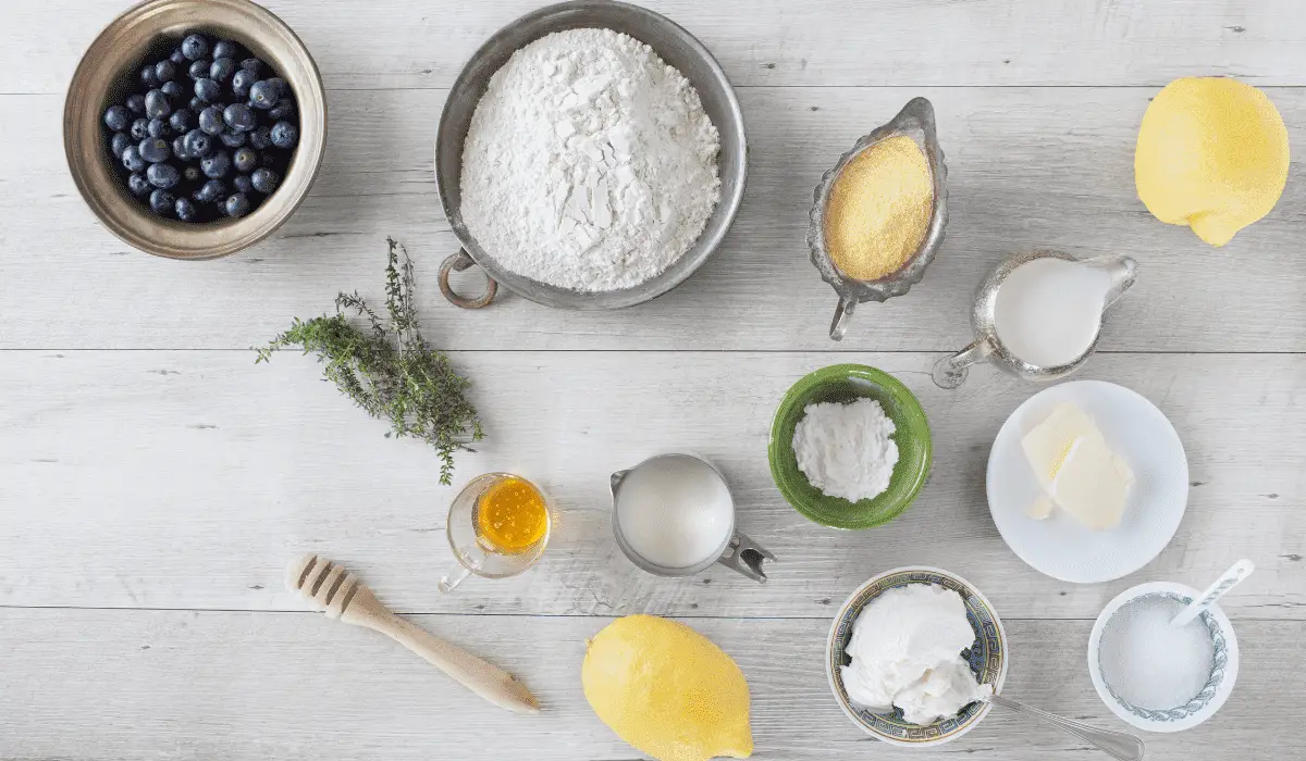 Array of fresh ingredients including blueberries, lemons, flour, eggs, and milk, ready for making lemon blueberry pancakes.