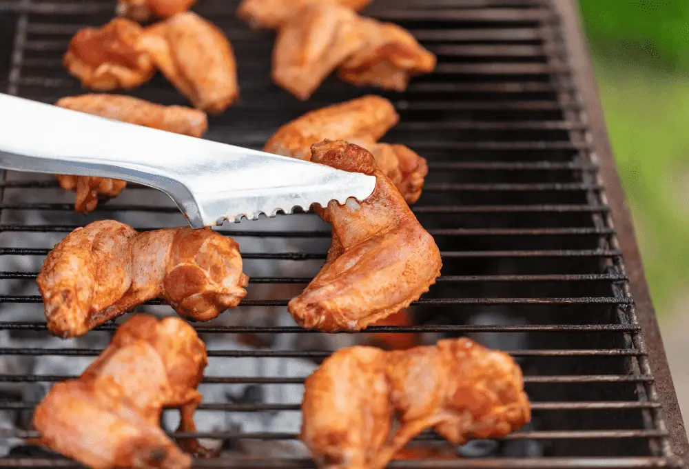 Fresh, uncooked chicken wings being placed onto a hot charcoal grill, ready for grilling.