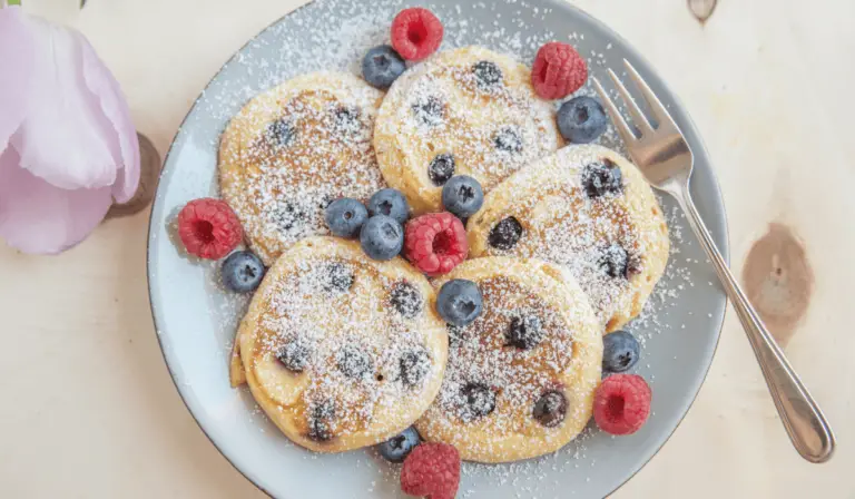 Fluffy lemon blueberry pancakes stacked high, drizzled with syrup, and garnished with fresh blueberries and lemon zest.
