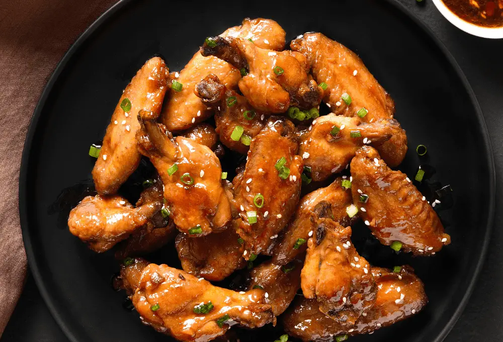 Platter of honey soy glazed chicken wings, garnished with sesame seeds and green onions.