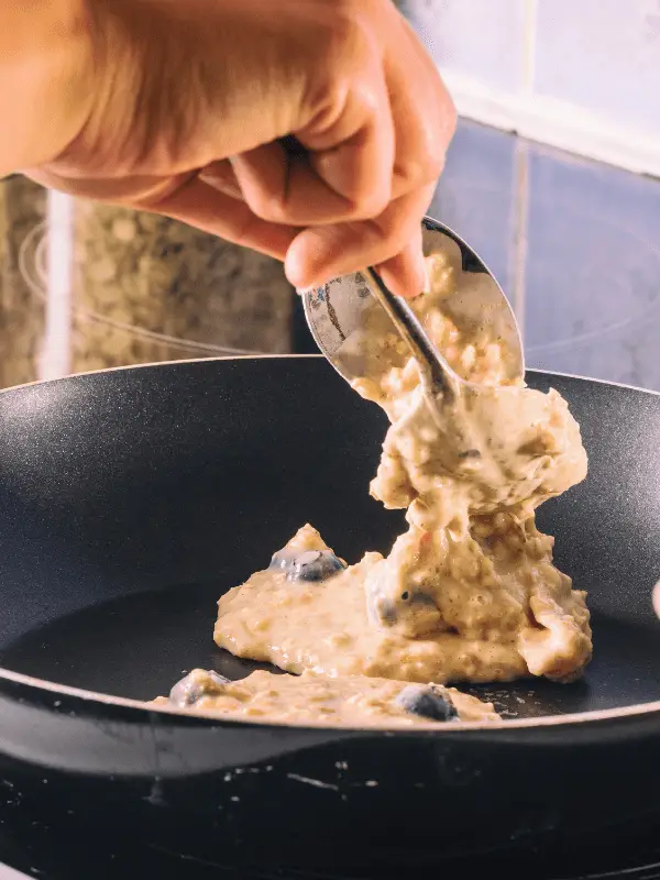 Batter being poured onto a hot skillet, with pancakes browning at the edges and blueberries peeking through.