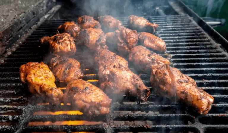Golden-brown chicken wings sizzling on a charcoal grill, with wisps of smoke rising