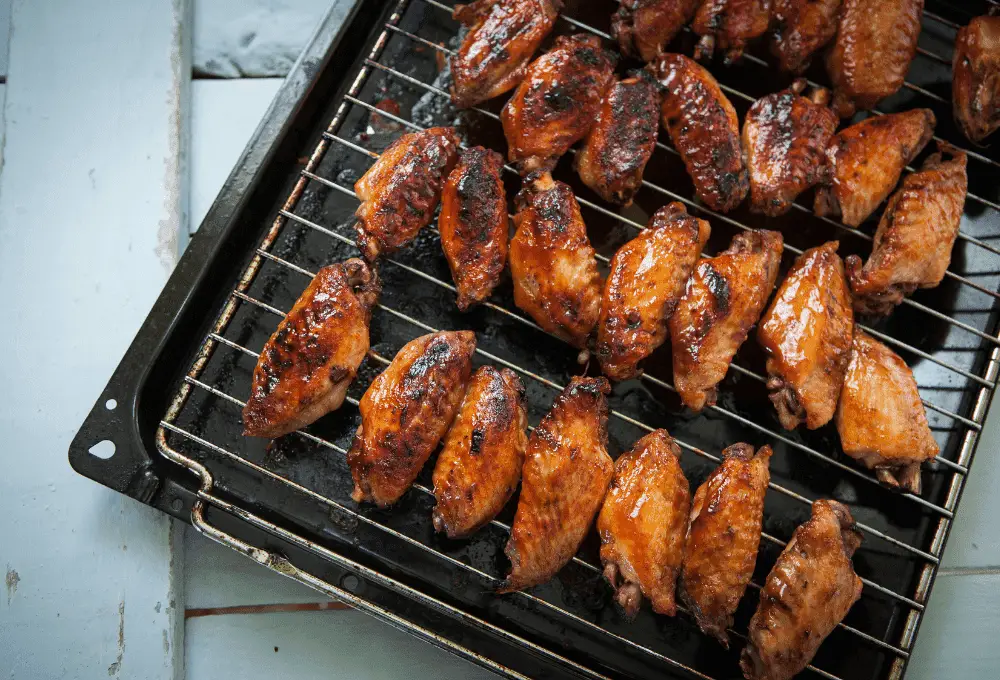 Brushing a glossy, rich sauce onto the grilling chicken wings, giving them a shiny and appetizing glaze.