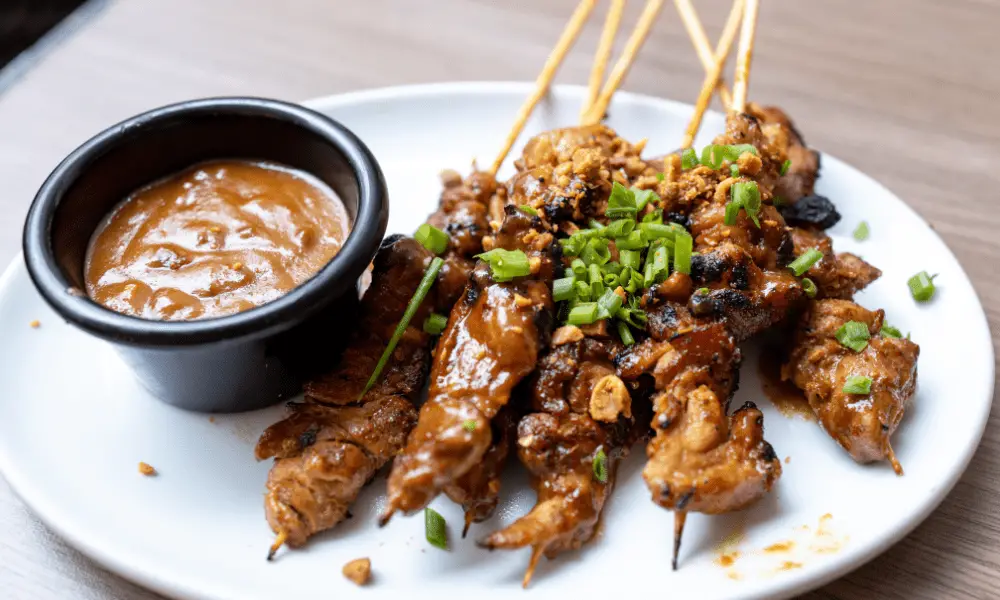 Chicken skewers on a plate, complemented by a side of rich peanut stir-fry sauce for dipping.