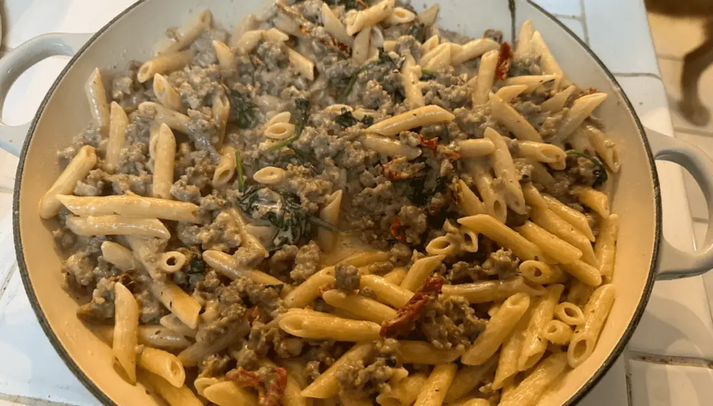 Creamy Tuscan sausage pasta garnished with fresh basil, parsley, and grated Parmesan cheese.