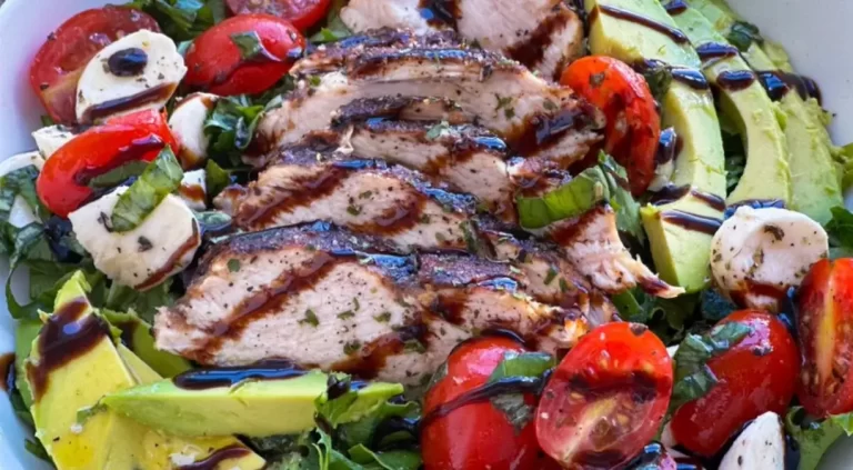 Juicy Caprese chicken paired with a vibrant rustic avocado salad, garnished with fresh basil and drizzled with balsamic glaze on a white plate.