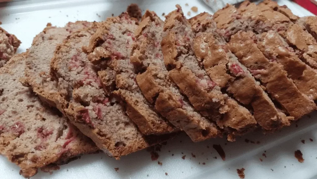 Sliced strawberry bread revealing moist and fluffy inside, arranged on a white plate.