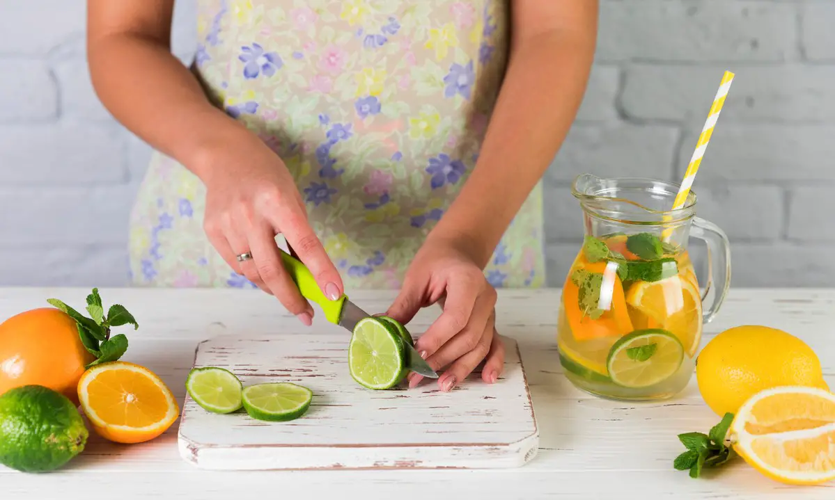 Focused woman meticulously slicing fresh fruits on a wooden cutting board, preparing ingredients for the lemon infused water.