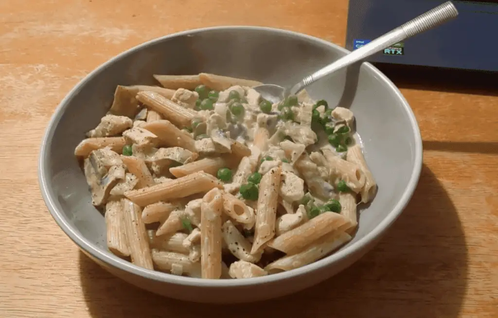 Creamy pasta dish garnished with fresh mushrooms, green peas, and a sprinkle of parmesan cheese.