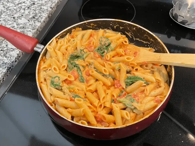 Stirring creamy tomato and spinach sauce with pasta in a skillet, capturing the rich blend of ingredients.