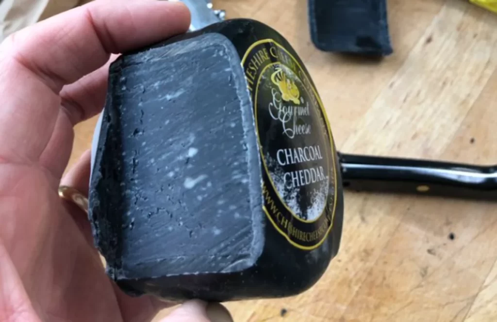 Close-up of a slice of mysterious black cheese with a charcoal hue, placed on a rustic wooden board.