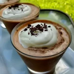 Chilled glass of frozen hot chocolate topped with whipped cream, set against a summer backdrop.