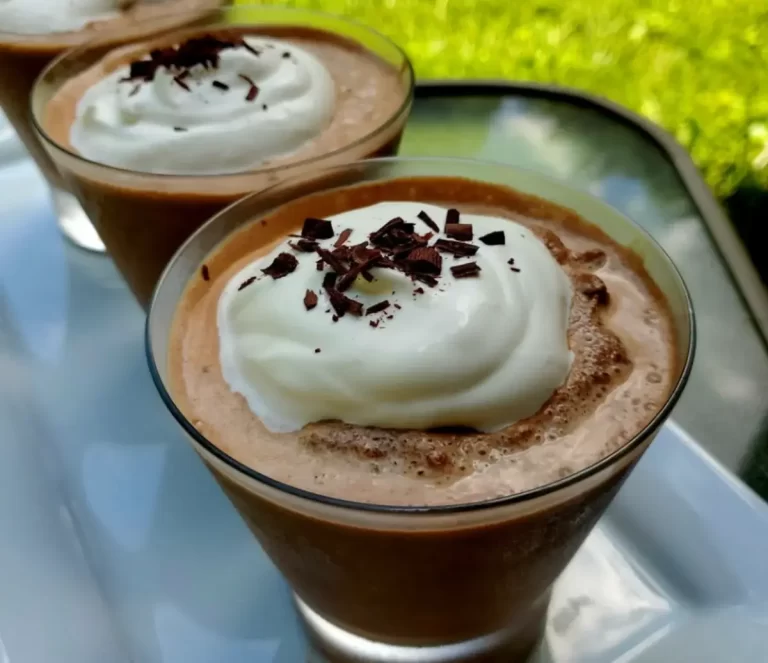 Chilled glass of frozen hot chocolate topped with whipped cream, set against a summer backdrop.