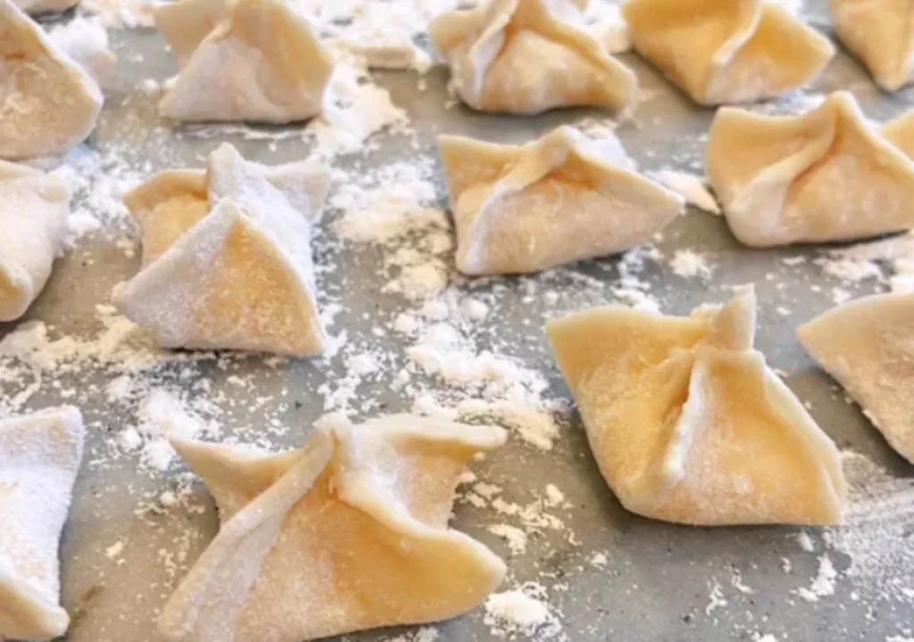 Freshly made sacchetti pasta arranged neatly on a wooden surface, with a sprinkle of flour and a rolling pin in the background.