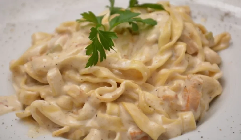 Delicious bowl of Pasta Alfredo con Pollo with creamy sauce, tender chicken, and garnished with parsley.