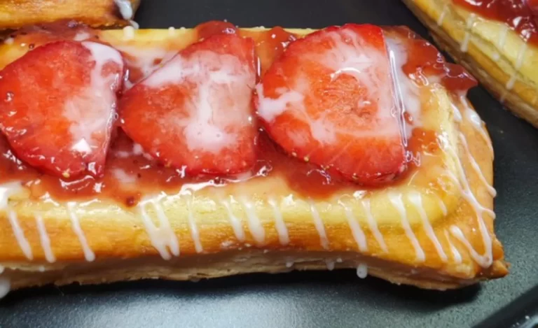 Delicious slice of Strawberry Cream Cheese Danish on a white plate with fresh strawberries on the side.