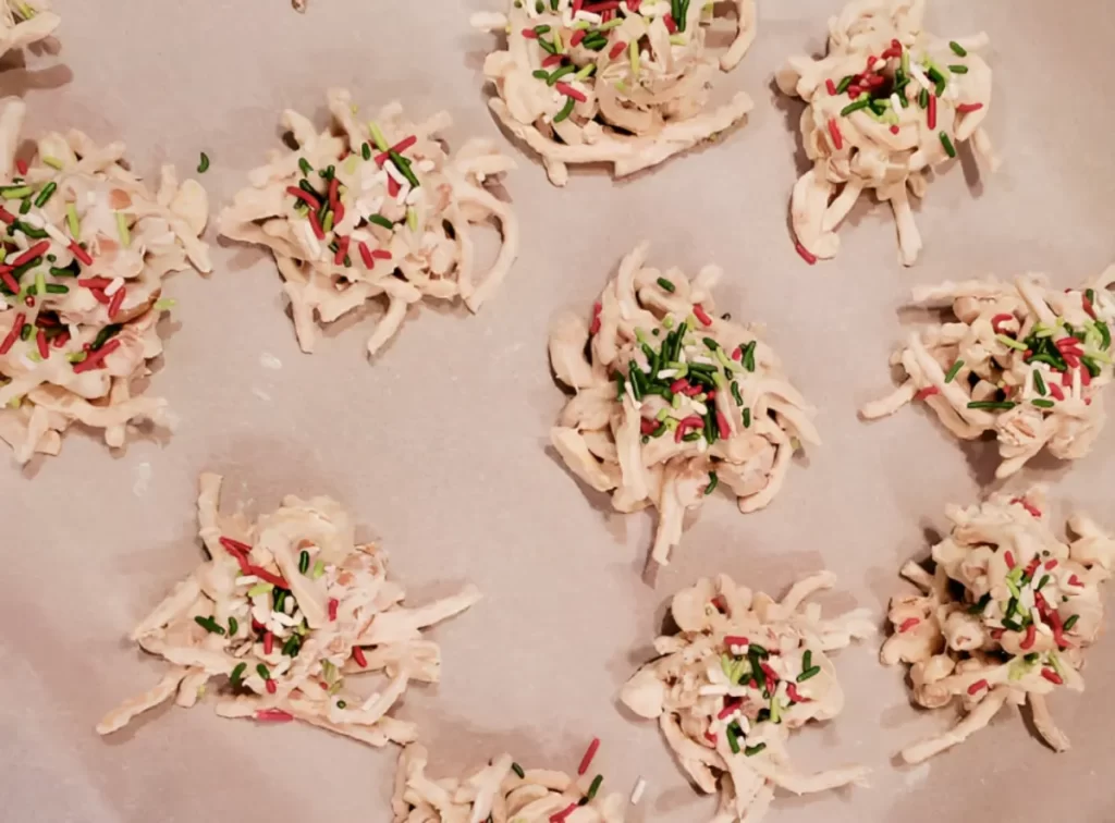 Deliciously stacked White Chocolate Haystacks on a festive plate, made with chow mein noodles and peanuts, coated in a glossy white marshmallow mixture, and sprinkled with colorful holiday nonpareils.