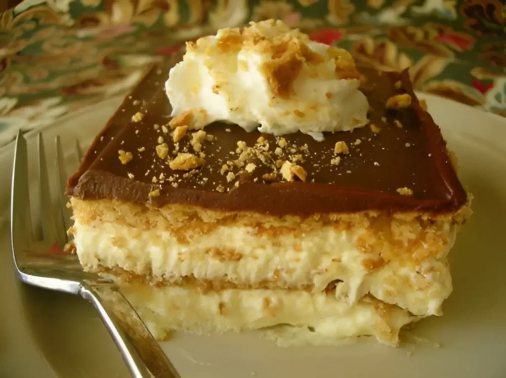 Delicious no-bake Chocolate Eclair Cake with layers of graham crackers, creamy pudding, and rich chocolate frosting, served on a white plate.