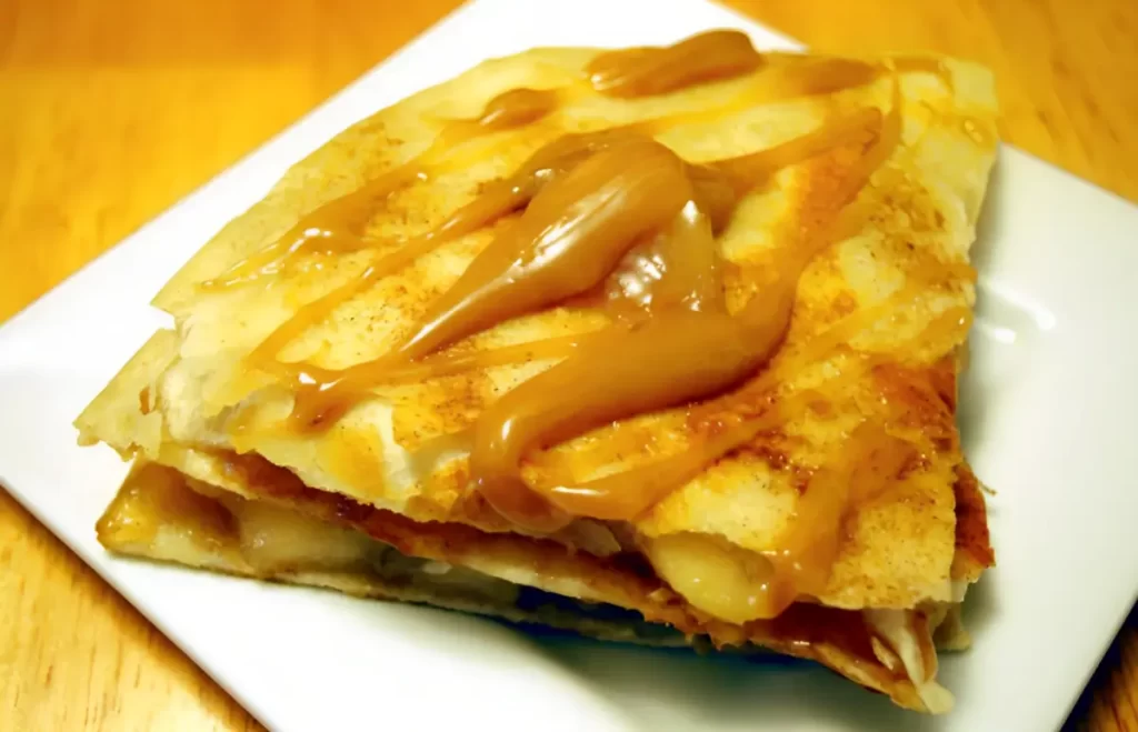 Crispy quesadilla filled with sweet apple pie mixture, drizzled with caramel on a white plate.