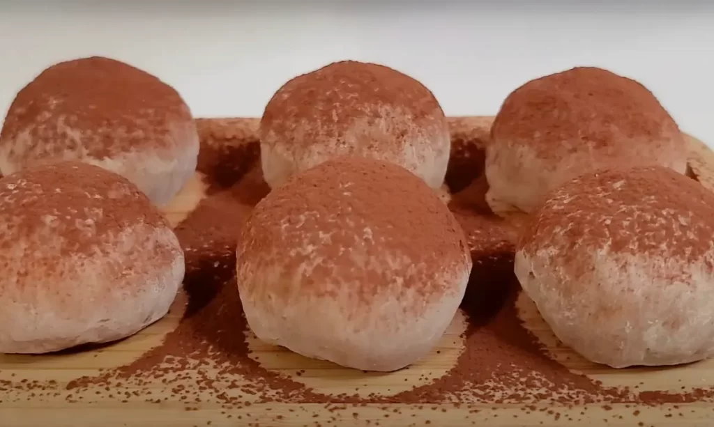 Close-up image of Tiramisu Ice Cream Mochi, with a cocoa-dusted exterior revealing a creamy coffee-flavored ice cream center, placed on a white plate.