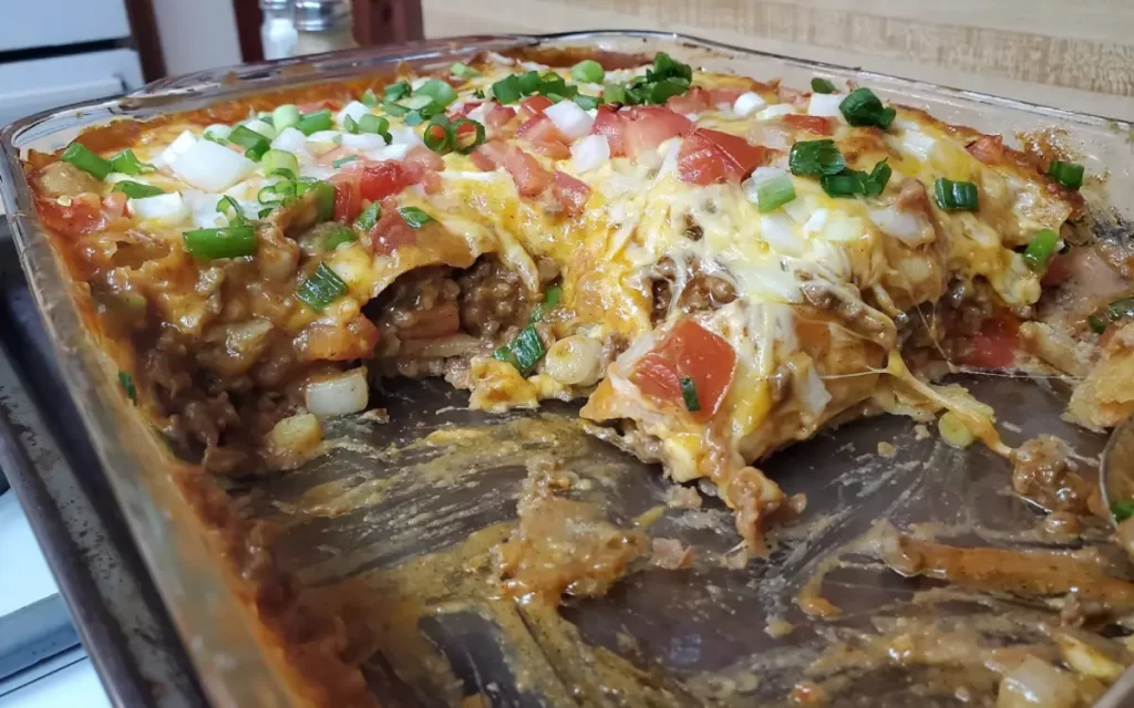 Delicious slice of Mexican Lasagna on a pan, showcasing the tempting layers of tortillas, seasoned beef, refried beans, and melted cheese, garnished with fresh cilantro.