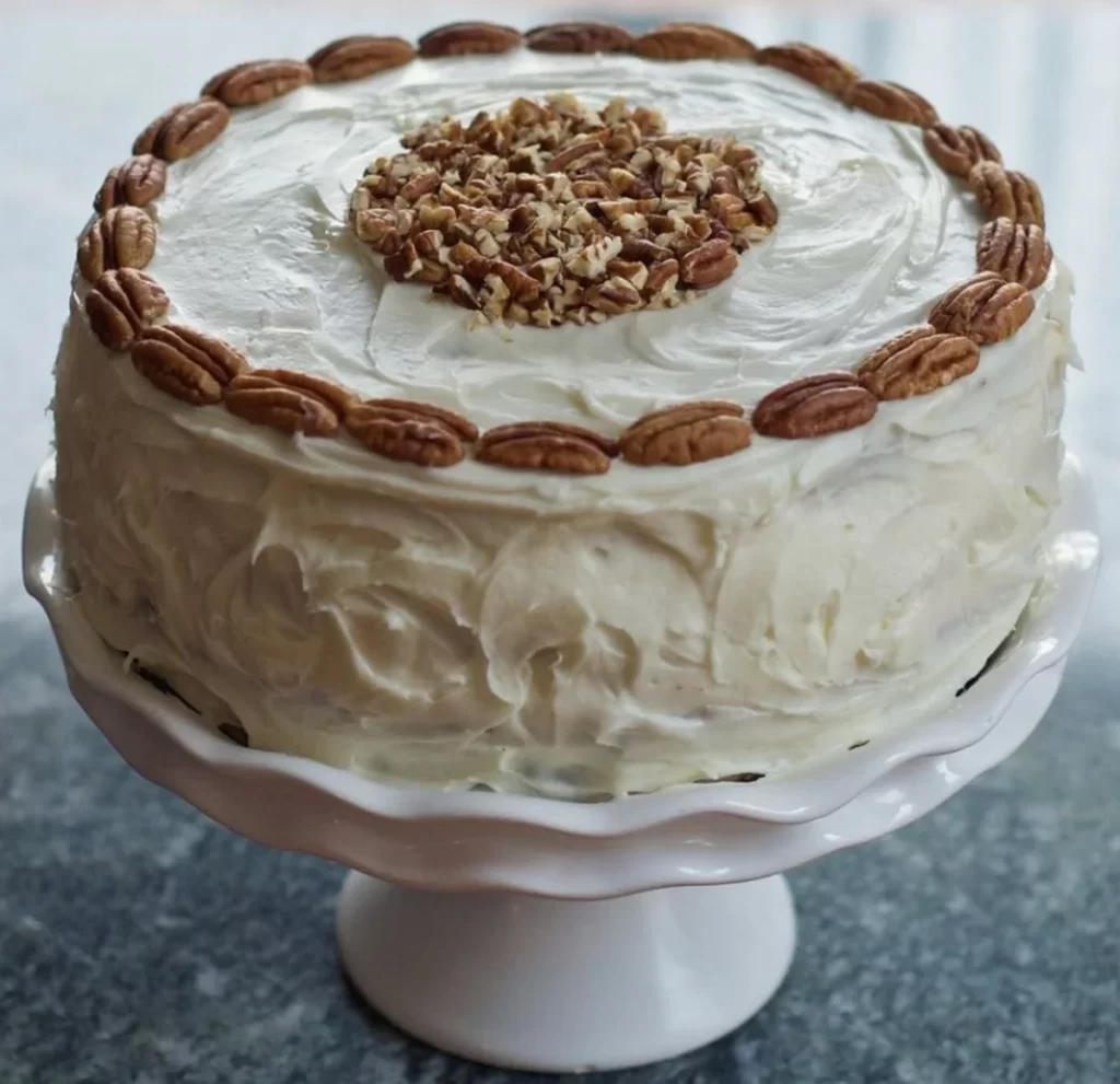 Delicious Hummingbird Cake with cream cheese frosting, garnished with toasted pecans on a serving plate.