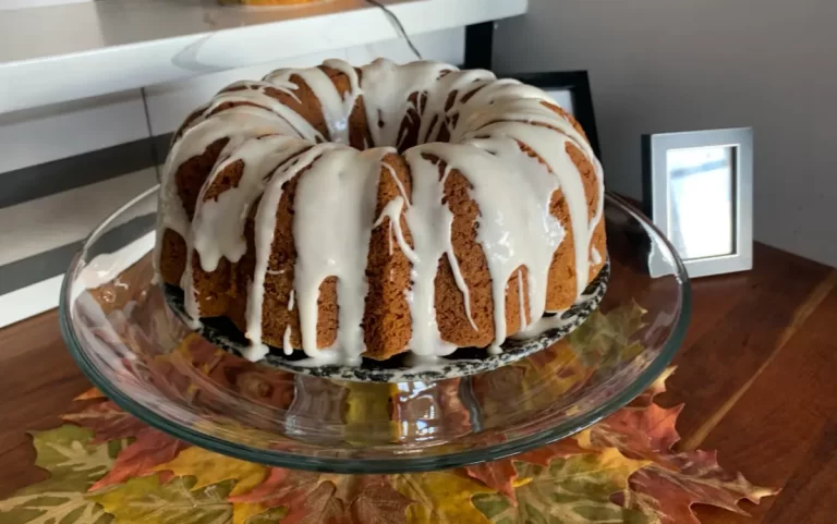 Delicious and moist Pumpkin Spice Bundt Cake with a sweet maple glaze on a white plate, surrounded by autumn leaves.