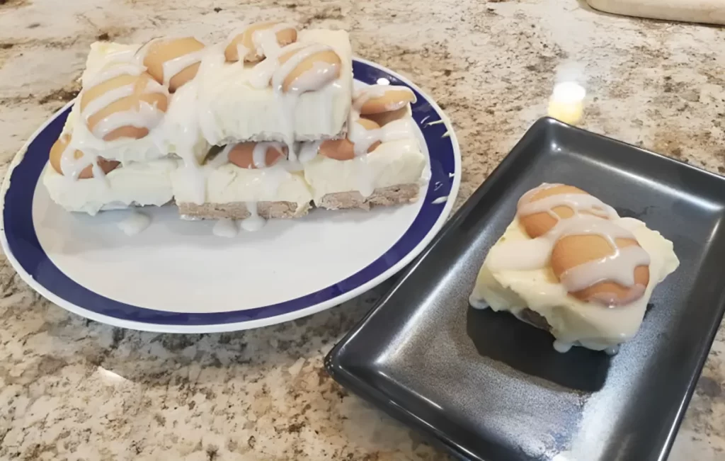 Creamy Banana Pudding Cheesecake Squares with a blondie crust, garnished with Nilla wafers on a white plate.