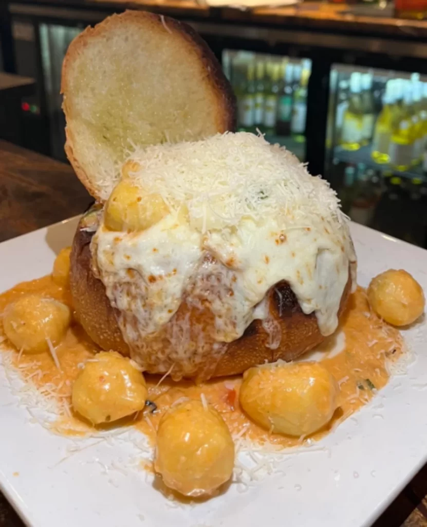 Delicious Stuffed Gnocchi Bomb in a bread bowl, topped with melted mozzarella and pink sauce, garnished with fresh basil.