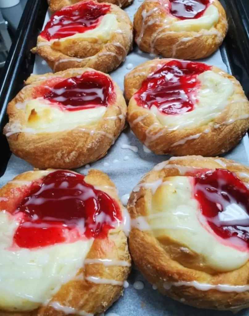 A delicious Strawberry Cream Cheese Danish on a white plate, garnished with fresh strawberries and a drizzle of glaze.