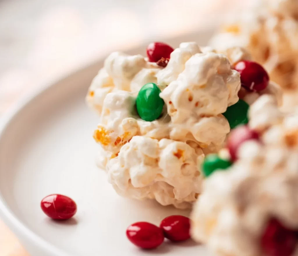 Christmas Popcorn Balls decorated with colorful M&Ms and sprinkles on a festive plate.