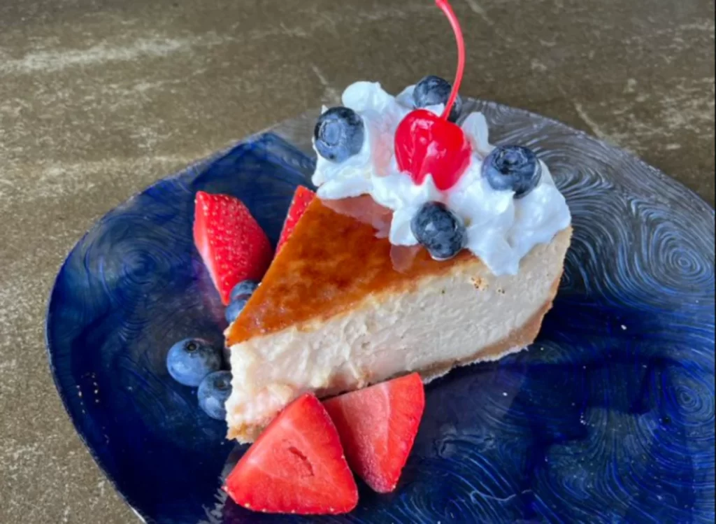 Delicious slice of salted caramel cheesecake on a blue plate, garnished with bluberries, strawberries, and cream chantilly.