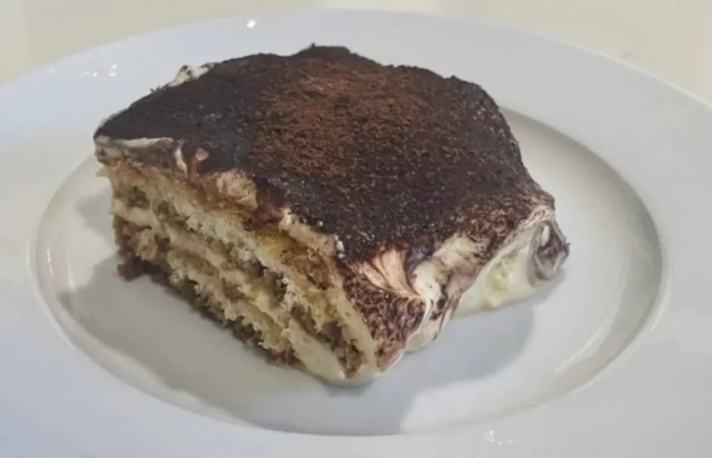 Close-up view of a layered Dark Chocolate Tiramisu dessert garnished with cocoa powder and chocolate shavings, served in a glass dish.