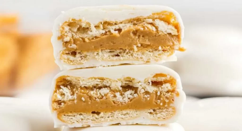 A close-up view showing the inside of a no-bake treat made from a Ritz cracker filled with peanut butter and coated in white chocolate.