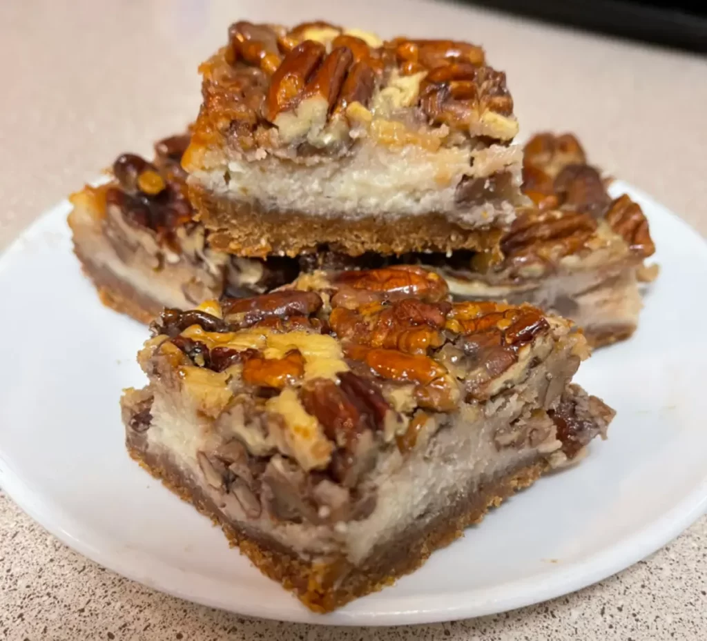 A delicious slice of Pecan Pie Cheesecake Bars showcasing layers of graham cracker crust, creamy cheesecake, and a rich pecan pie topping.