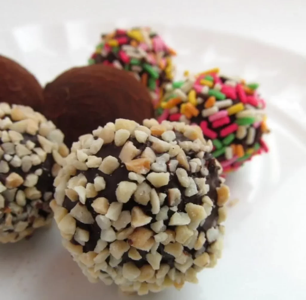 Homemade chocolate truffles coated with nuts and sprinkles on a white plate.