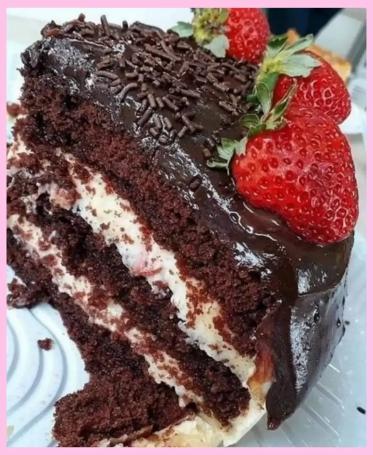 A slice of moist chocolate cake with cream and strawberries topped with chocolate ganache.