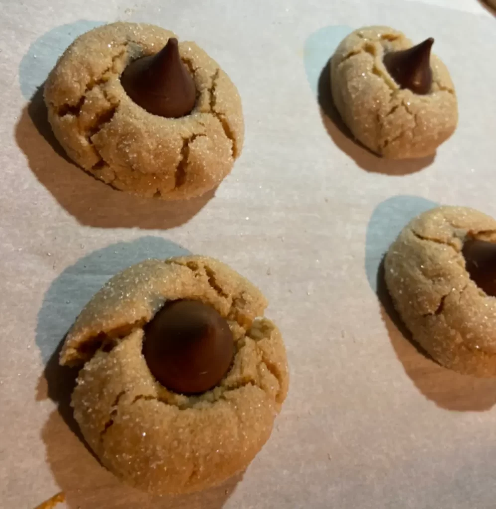 A plate of freshly baked Peanut Butter Blossom Cookies, each topped with a chocolate kiss.