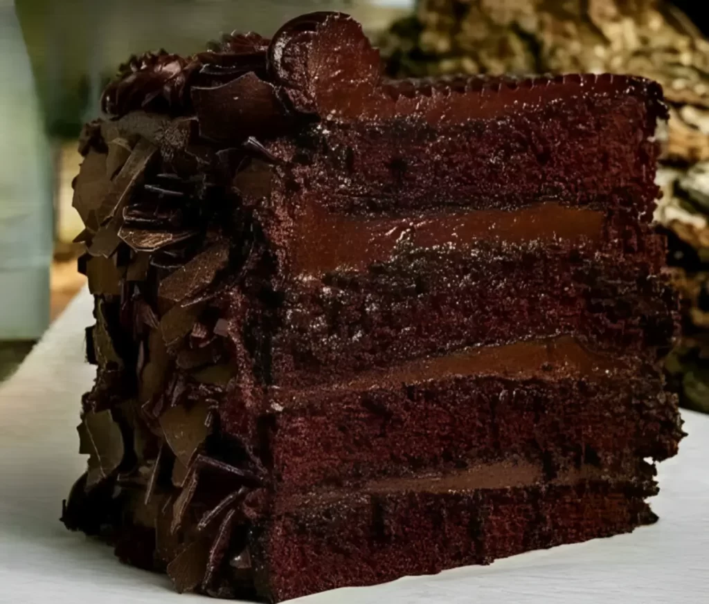 Slice of decadent multi-layer chocolate cake with silky chocolate ganache frosting and chocolate curls on top