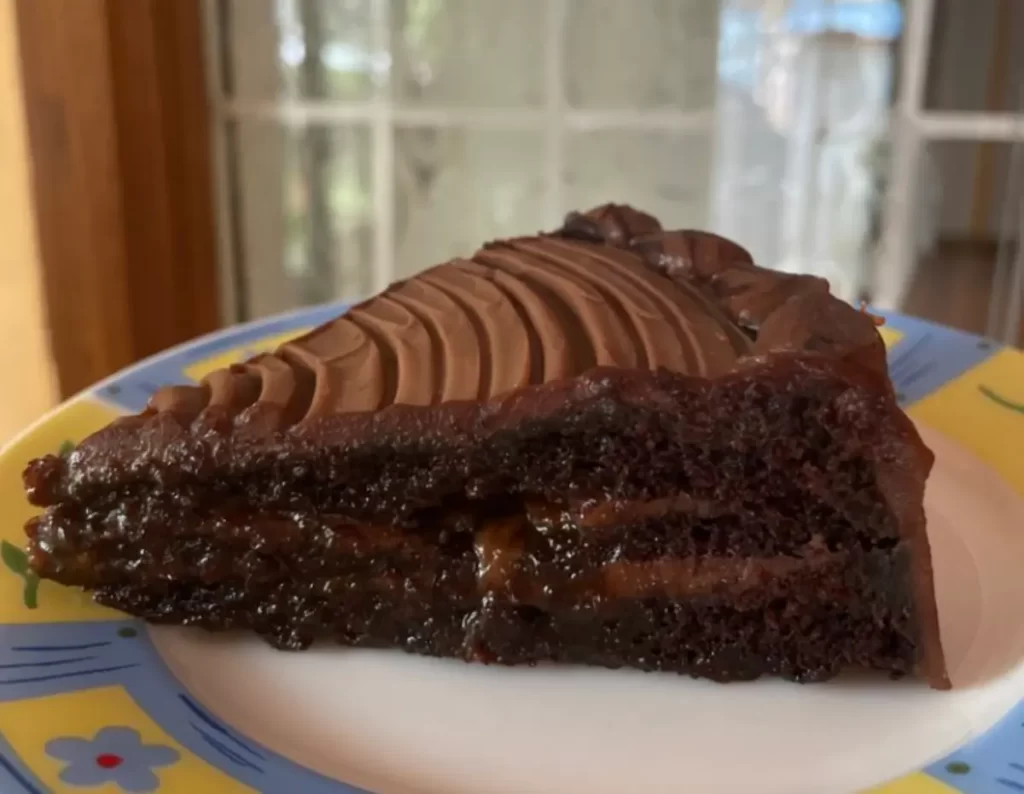 A slice of Gooey Chocolate Cake with rich frosting on a plate, showcasing its moist and dense texture with a shiny ganache center.