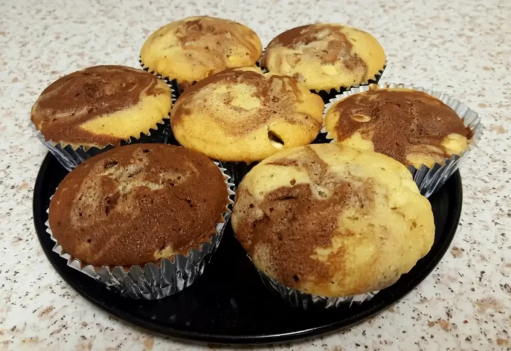 A close-up of freshly baked Marble Muffins, showcasing the swirls of vanilla and chocolate.