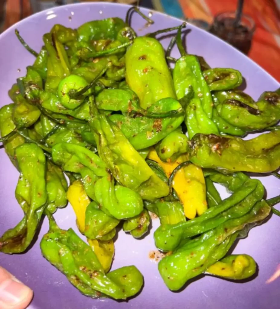 Charred green shishito peppers on a purple plate, ready to be enjoyed as a spicy-sweet snack.